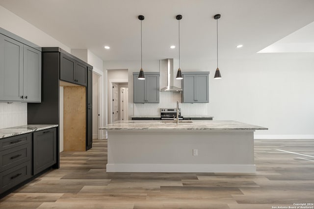 kitchen featuring a center island with sink, hanging light fixtures, and wall chimney range hood