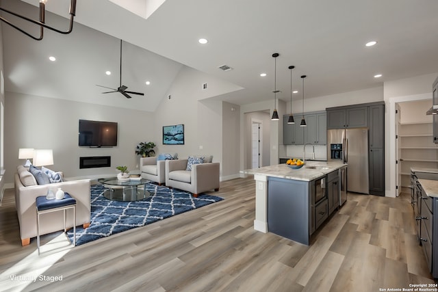 kitchen with sink, stainless steel fridge, decorative light fixtures, gray cabinets, and a kitchen island with sink