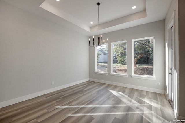 unfurnished dining area featuring light wood-type flooring, a tray ceiling, and a notable chandelier