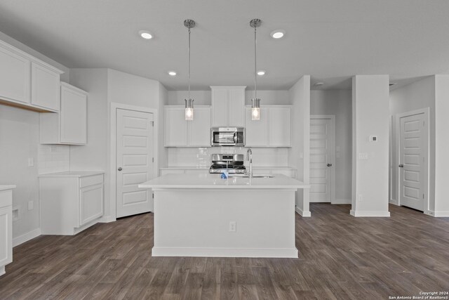 kitchen with white cabinets, appliances with stainless steel finishes, decorative light fixtures, and an island with sink