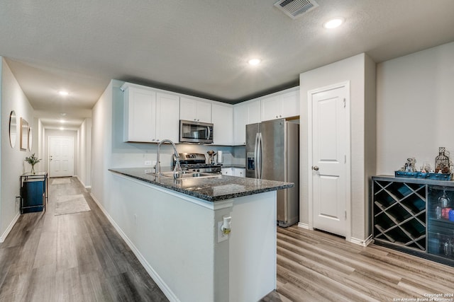 kitchen featuring kitchen peninsula, dark stone countertops, appliances with stainless steel finishes, light hardwood / wood-style floors, and white cabinetry