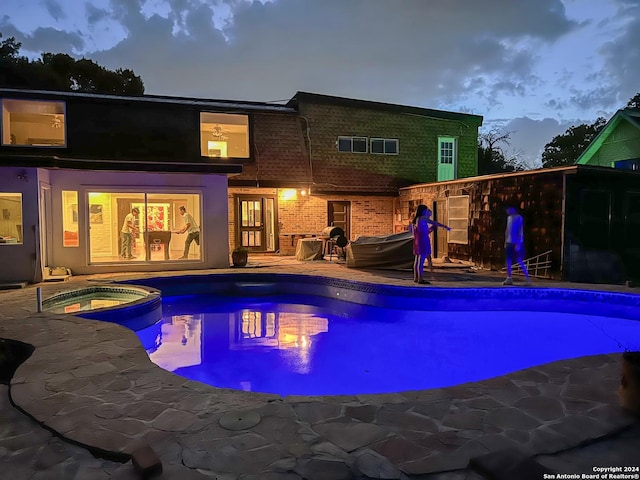 pool at dusk with an in ground hot tub and a patio