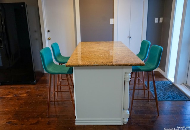 kitchen with black fridge, dark hardwood / wood-style floors, a kitchen island, light stone counters, and a breakfast bar area