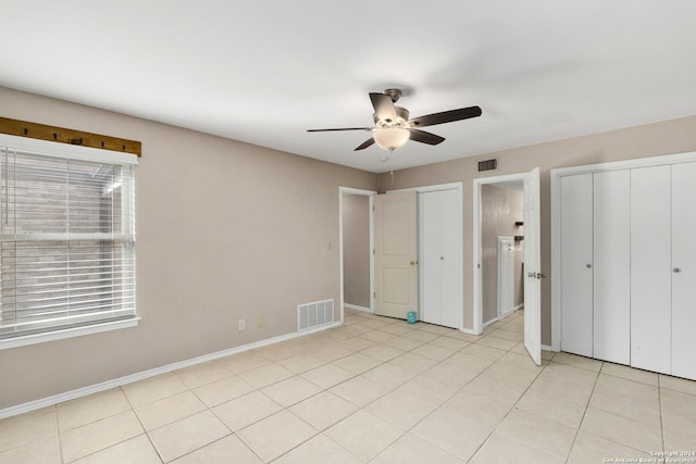 unfurnished bedroom with ceiling fan, light tile patterned flooring, and two closets