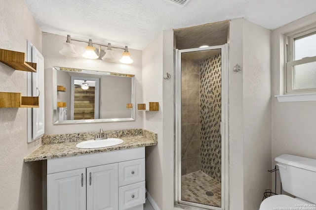 bathroom featuring ceiling fan, a textured ceiling, toilet, vanity, and a shower with shower door