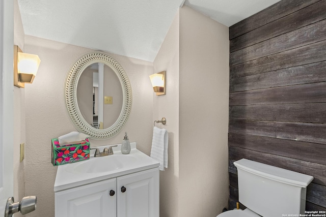 bathroom featuring wood walls, vanity, a textured ceiling, and toilet