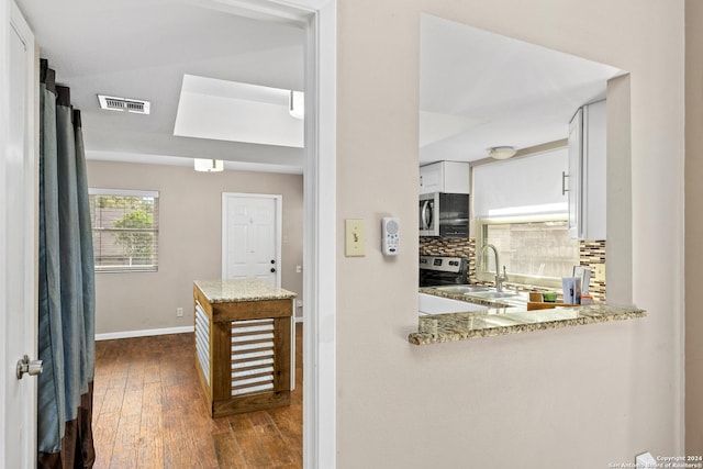 kitchen featuring white cabinetry, dark wood-type flooring, stainless steel appliances, light stone counters, and backsplash