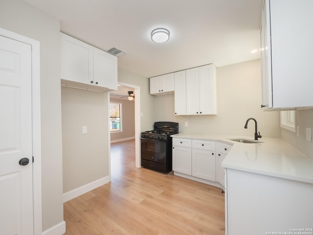 kitchen with light wood-type flooring, gas stove, ceiling fan, sink, and white cabinets