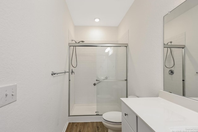 bathroom with hardwood / wood-style floors, vanity, toilet, and a shower with shower door