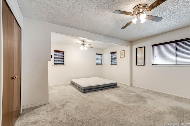 unfurnished bedroom featuring ceiling fan, a textured ceiling, light carpet, and a closet