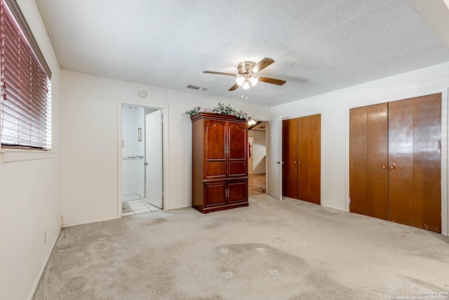 unfurnished bedroom featuring light carpet, two closets, ensuite bathroom, ceiling fan, and a textured ceiling