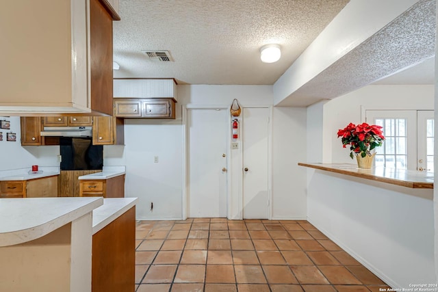 kitchen with kitchen peninsula, a textured ceiling, and light tile patterned flooring