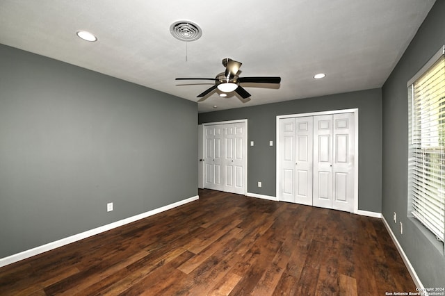 unfurnished bedroom with multiple closets, ceiling fan, and dark wood-type flooring