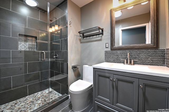 bathroom featuring vanity, toilet, a shower with door, and tasteful backsplash