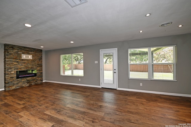 unfurnished living room with a stone fireplace, plenty of natural light, and dark hardwood / wood-style flooring