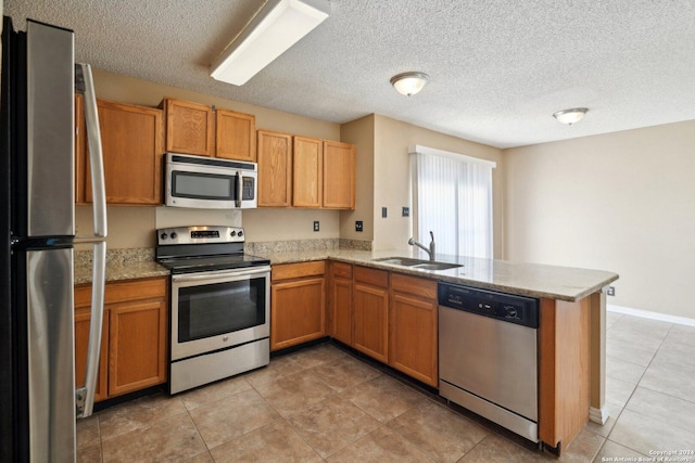 kitchen featuring sink, stainless steel appliances, light stone counters, kitchen peninsula, and a textured ceiling