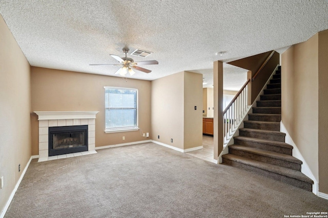 unfurnished living room with ceiling fan, a fireplace, light colored carpet, and a textured ceiling