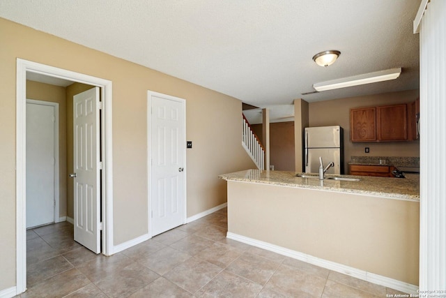 kitchen with stainless steel refrigerator, sink, light stone counters, kitchen peninsula, and a textured ceiling