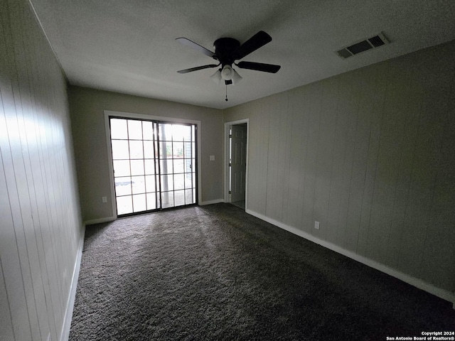 empty room featuring dark carpet, wooden walls, a textured ceiling, and ceiling fan