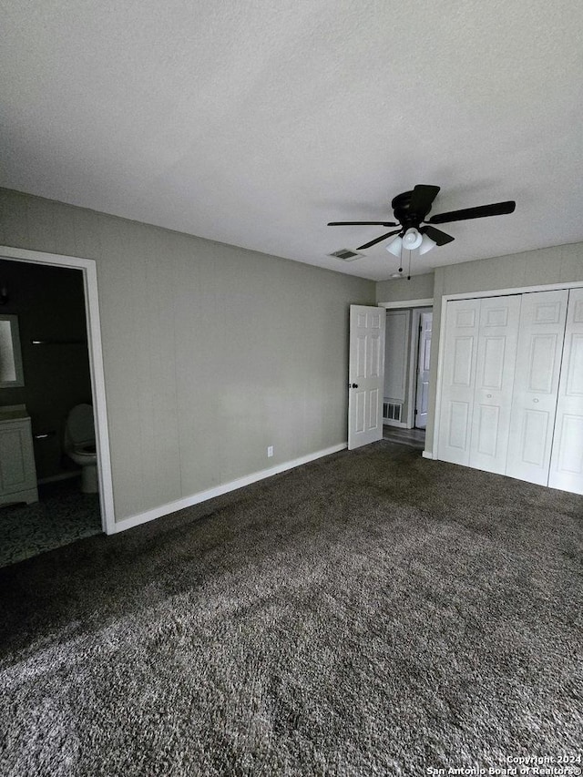 unfurnished bedroom with dark colored carpet, ensuite bathroom, a textured ceiling, and ceiling fan