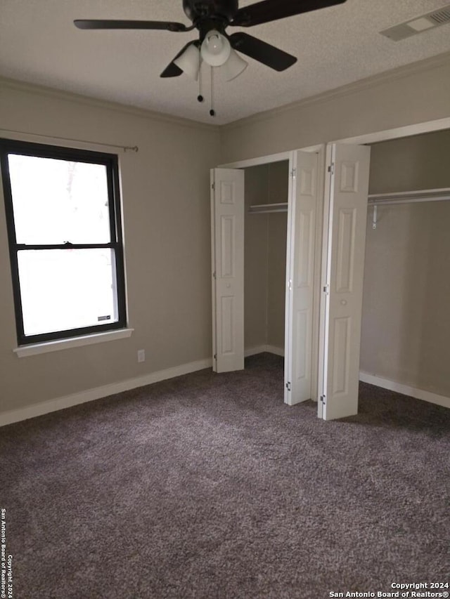 unfurnished bedroom with multiple closets, ornamental molding, carpet floors, and ceiling fan