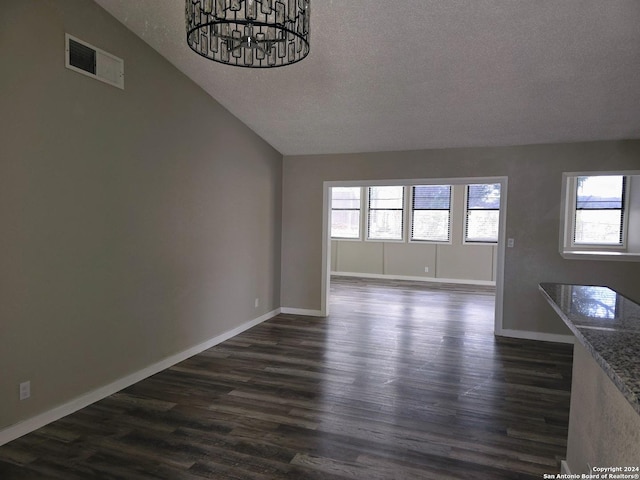 unfurnished living room with lofted ceiling, dark hardwood / wood-style floors, a chandelier, and a textured ceiling