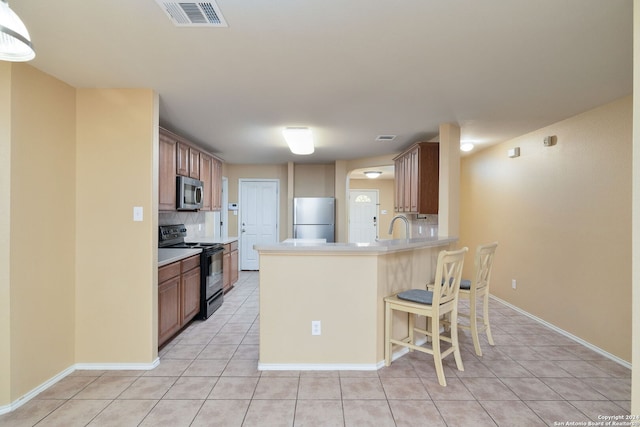 kitchen featuring kitchen peninsula, backsplash, stainless steel appliances, light tile patterned floors, and a breakfast bar area