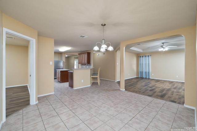 kitchen with kitchen peninsula, stainless steel fridge, pendant lighting, light tile patterned floors, and ceiling fan with notable chandelier