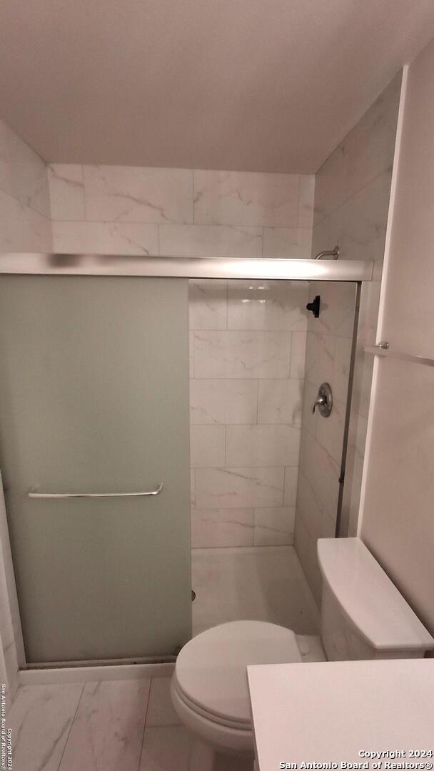 full bath with marble finish floor, a shower stall, and toilet