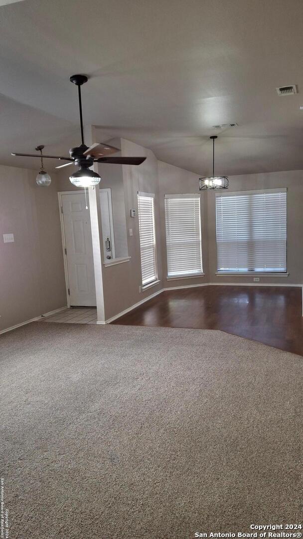 unfurnished room with carpet, visible vents, vaulted ceiling, baseboards, and ceiling fan with notable chandelier