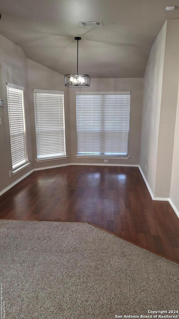 unfurnished dining area with dark wood-style flooring, a notable chandelier, visible vents, vaulted ceiling, and baseboards