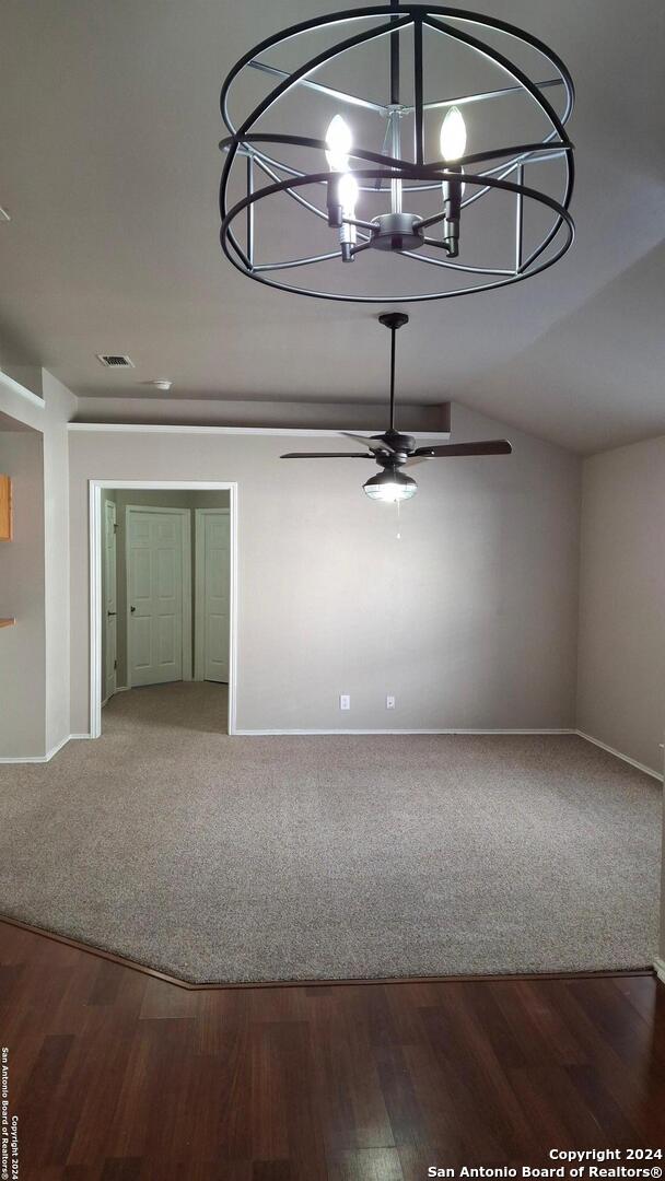 spare room featuring visible vents, carpet flooring, vaulted ceiling, baseboards, and ceiling fan with notable chandelier