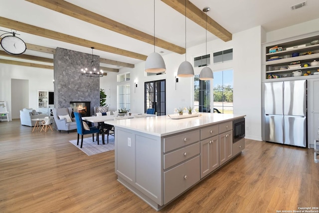 kitchen with stainless steel fridge, black microwave, beam ceiling, decorative light fixtures, and a center island