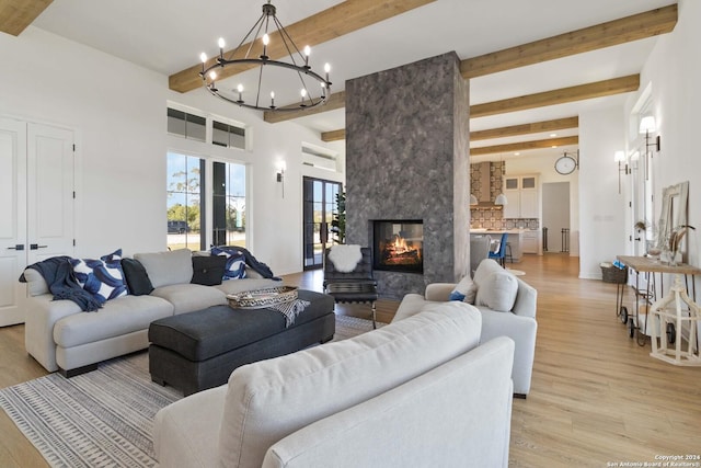 living room featuring beamed ceiling, light wood-type flooring, an inviting chandelier, and a multi sided fireplace