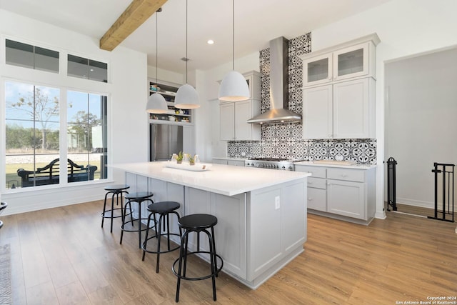 kitchen featuring stove, hanging light fixtures, wall chimney exhaust hood, beam ceiling, and a kitchen island