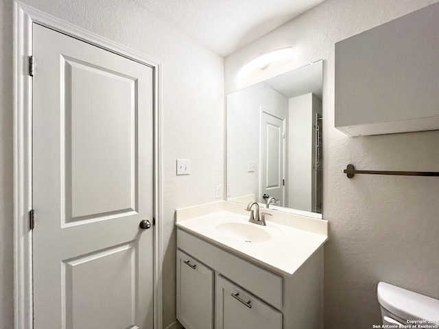 bathroom with a textured ceiling, vanity, and toilet