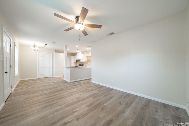 unfurnished living room with ceiling fan with notable chandelier and light hardwood / wood-style flooring