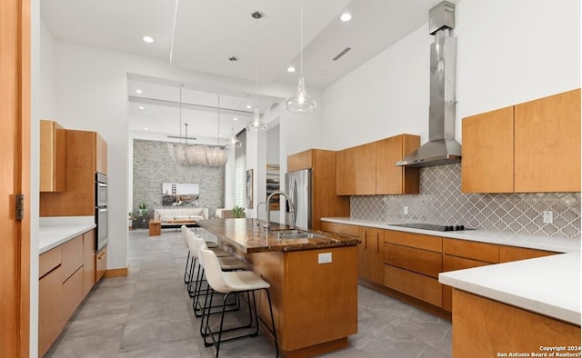 kitchen with sink, hanging light fixtures, wall chimney range hood, a kitchen breakfast bar, and a spacious island