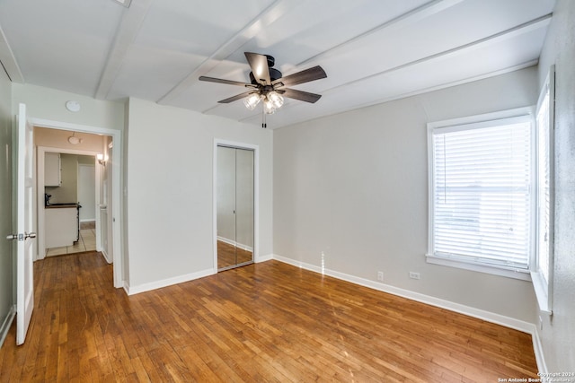 unfurnished bedroom featuring hardwood / wood-style flooring, ceiling fan, beamed ceiling, and a closet