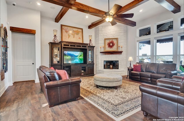 living room with beamed ceiling, ceiling fan, a stone fireplace, and dark wood-type flooring