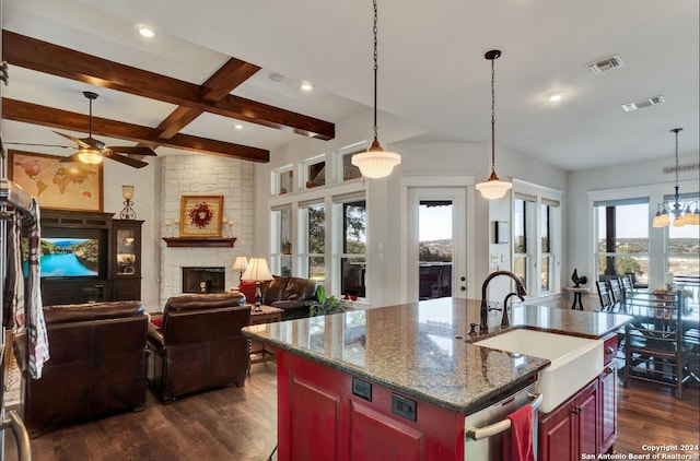 kitchen with light stone countertops, a fireplace, sink, a center island with sink, and beamed ceiling