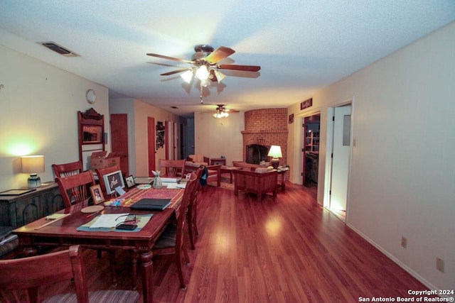 dining space featuring a textured ceiling, hardwood / wood-style flooring, and a brick fireplace