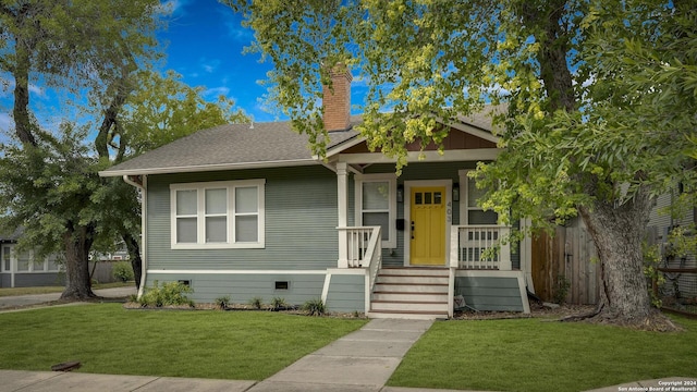 bungalow-style home with covered porch, roof with shingles, crawl space, a chimney, and a front yard