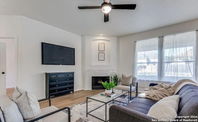 living room with ceiling fan, light hardwood / wood-style flooring, and a brick fireplace