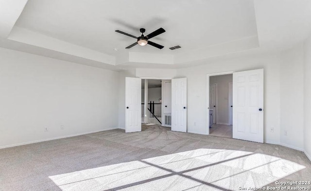 unfurnished bedroom featuring light carpet, a tray ceiling, and ceiling fan