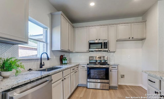 kitchen with light stone counters, light hardwood / wood-style floors, sink, and stainless steel appliances