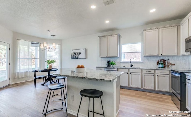 kitchen featuring light stone countertops, appliances with stainless steel finishes, light wood-type flooring, an inviting chandelier, and a kitchen island