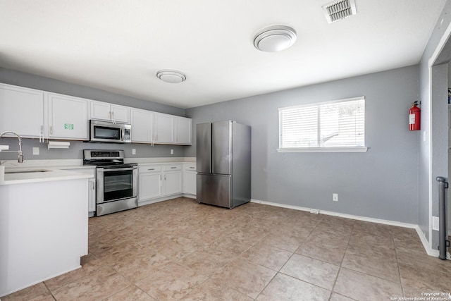 kitchen with appliances with stainless steel finishes, light tile patterned floors, white cabinetry, and sink