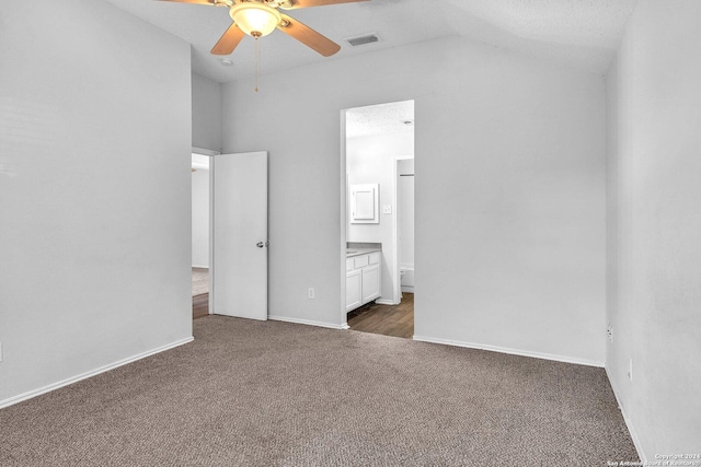 unfurnished bedroom featuring dark carpet, lofted ceiling, ensuite bath, ceiling fan, and a textured ceiling