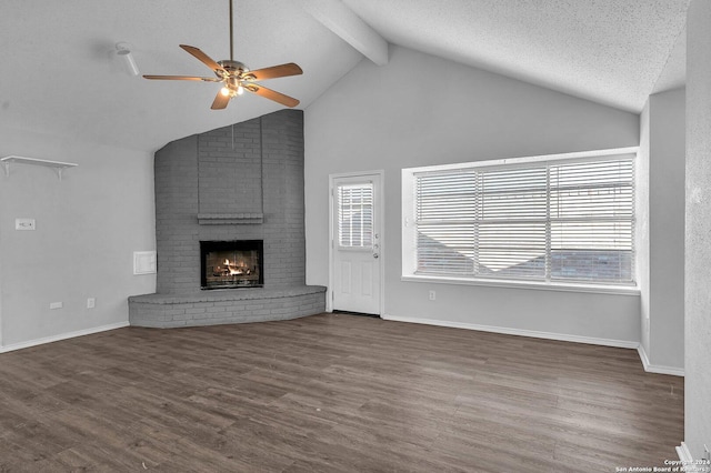 unfurnished living room with a brick fireplace, a textured ceiling, ceiling fan, lofted ceiling with beams, and dark hardwood / wood-style floors